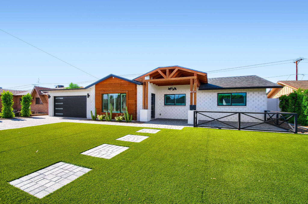 A modern single-story home with a vibrant green lawn, stone paver walkway, and a mix of white brick and natural wood siding. Photo by Virtuance.