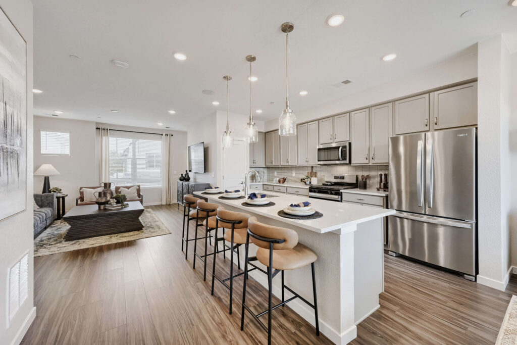 An open-concept kitchen and living area designed in neutral gray and tan tones with stainless steel appliances. Photo by Virtuance.
