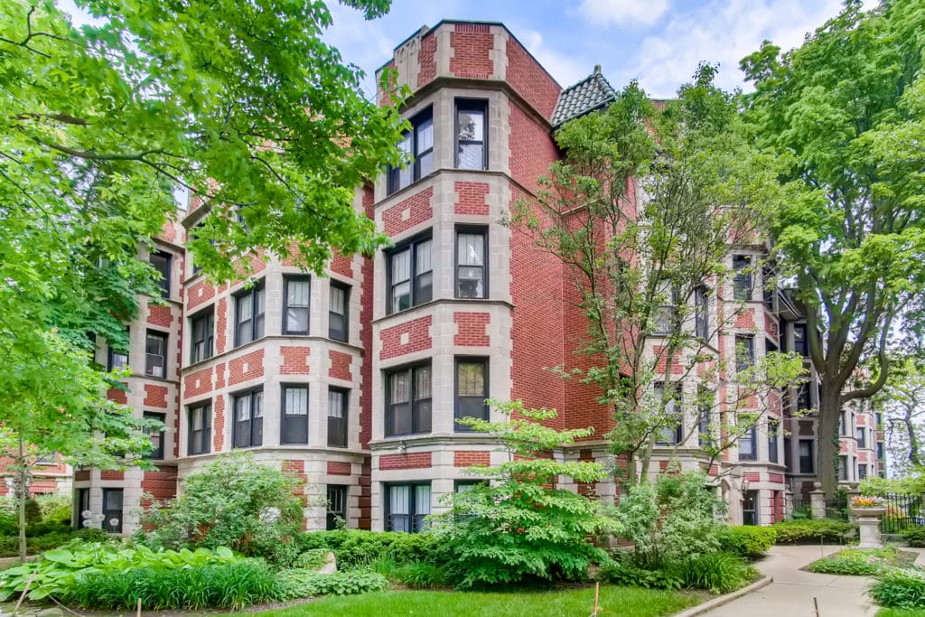 Luxury Lincoln Park multi-family condo complex with a timeless brick exterior, symmetrical black-framed windows, neat limestone trim, and a small wrought-iron fenced garden in front. Image capture by Virtuance